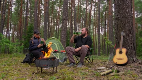 Couple camping in pine forest enjoying campfire and beer Stock Footage 327134830