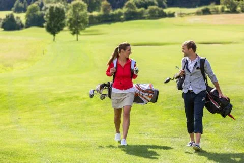 Couple carrying golf bag while walking on golf course Fotos de archivo