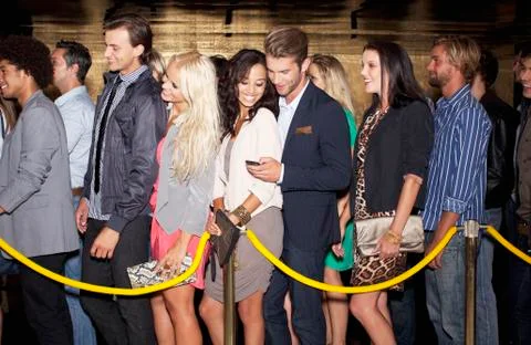 Couple with cell phone standing in queue outside nightclub Foto stock