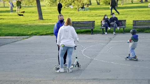 A couple chat in a park while another couple with surgical masks seat on a Vídeos de archivo 133207116