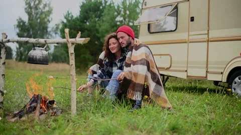 Couple in a checkered plaid roasting marshmallows on fire near the trailer home. 스톡 동영상 170675953