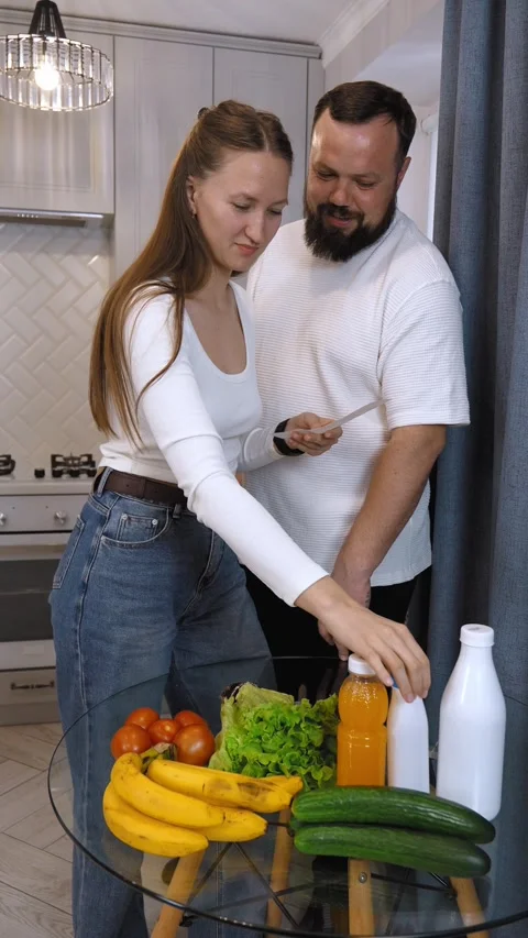 Couple checking grocery receipt and comparing with food items in kitchen Stock Footage 320492597