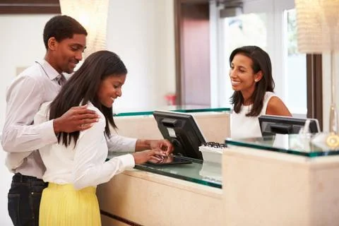 Couple Checking In At Hotel Reception Using Digital Tablet 写真素材