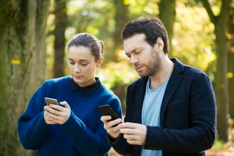 Couple checking smartphones while walking in woods Stock Photos