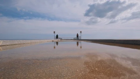Couple with a child walking on the pier, reflected in the puddle. Stock Footage 130027097