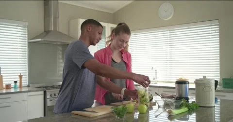 Couple chopping and adding greens into blender jar at kitchen island making Video stock 345071315