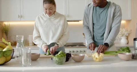 Couple chopping cucumbers and slicing pineapple at counter using cutting boards Stock Footage 345589734