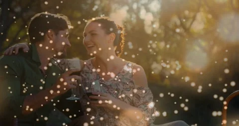 Couple clinking glasses in park, leaning in and kissing amid particles and lens 스톡 동영상 330355673