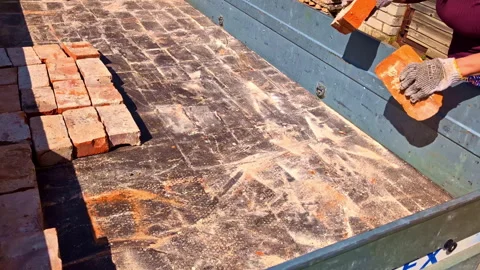 Couple collecting rough red bricks from back of flat bed trailer for building Stock Footage 314638223