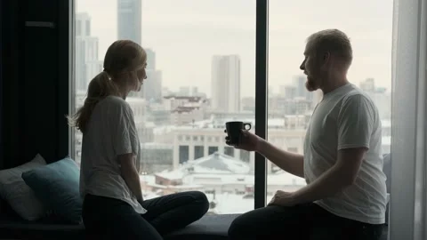 Couple communicates sitting on the windowsill by the window overlooking the city Video stock 135420487