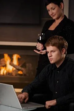 Couple with computer at home Young man sitting in front of fireplace at ho... Stock Photos