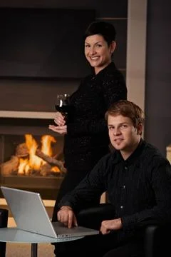 Couple with computer at home Young man sitting in front of fireplace at ho... Stock Photos