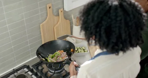 Couple cooking in kitchen with prepped veg, woman holding wok tossing stirfry as Stockbeeldmateriaal 344964869