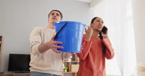 Couple coping with ceiling leak, man holds bucket as woman phones plumber Stock Footage 335096718