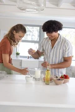 Couple cracking egg and stirring ingredients at modern home kitchen island with 스톡 사진