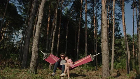 Couple cuddles lying on colourful hammock in pine forest Video stock 219953384