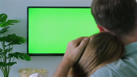 Couple cuddling on couch while watching green screen TV, popcorn in Stock Footage 285545420