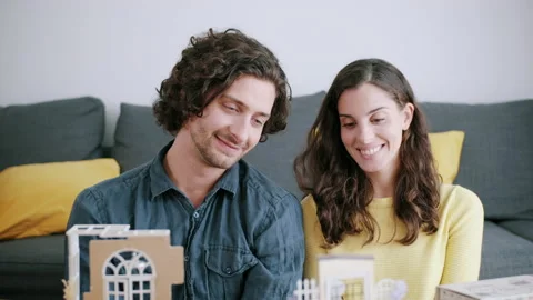 Couple cuddling while looking at miniature model house Stock Footage 130324864