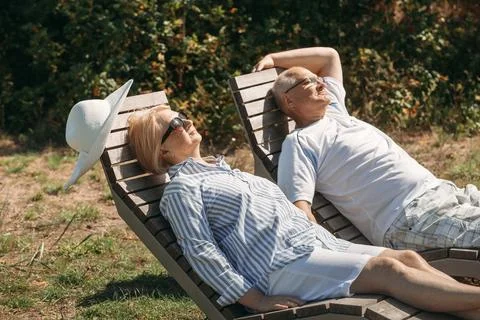 A couple of cute elderly people lie on sunbeds holding hands. Stock Photos