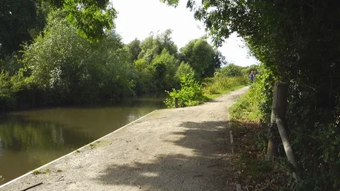 A couple of cyclists cycle down a path alongside the River Kennet. Stock Footage 114248818