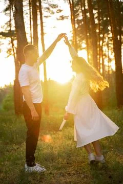 Couple dancing joyfully in a sun-drenched forest during golden hour Stock Photos
