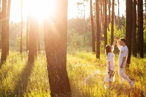 Couple dancing in a sun-drenched forest with tall trees and golden light Stock Photos