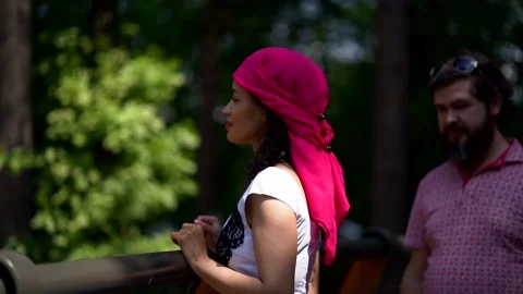 A couple: a dark-haired curly-haired girl and a man are in a green Park, looking Stock Footage 134842009