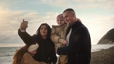 Couple with daughters taking selfies with their smartphone standing by the ocean Stock Footage 307594410