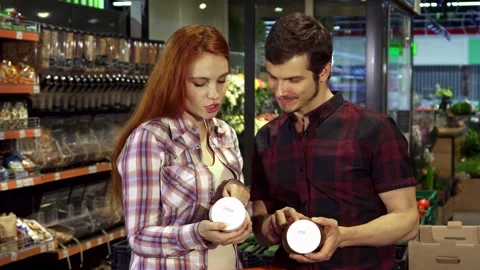 Couple debates over food composition labels in a vibrant supermarket Stock Footage 311990995