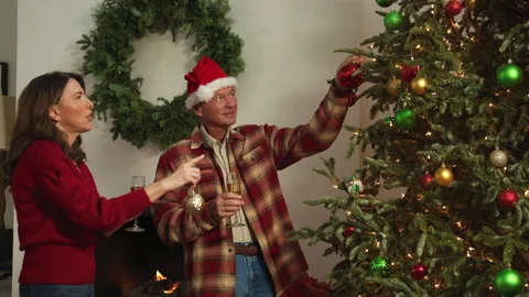 A couple decorates a Christmas tree and shares champagne near the fireplace. Stock Footage 340927825