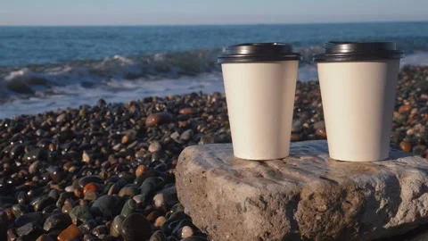 Couple of disposable white cups of coffee on beach by sea. Stock Footage 263762489