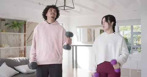 Couple doing biceps curls at home, man in pink hoodie straining with heavy Stock Footage 345090220