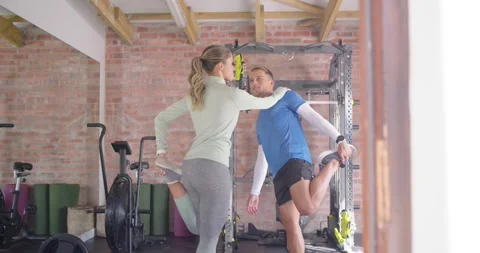 Couple doing quad stretch at home gym, woman reaching for balance, man bracing Stock Footage 342803522