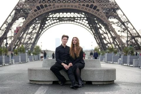 Couple dressed in black sits on bench near Eiffel Tower holding hands Stock Photos
