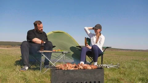 Couple drinking beer and grilling barbecue at campsite Видео 344605480