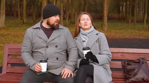 Couple drinking coffee and talking on a park bench Stock Footage 326146218