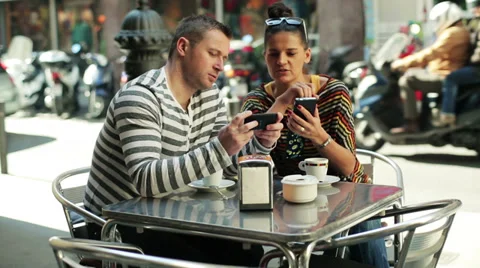 Couple drinking coffee and using cellphones by the table outside the cafe Stock-Footage 36837379