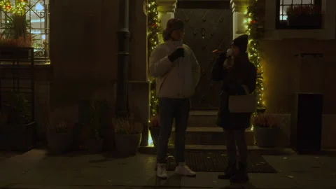 A couple drinking hot beverages from cups on a city street at night Stock Footage 311462834