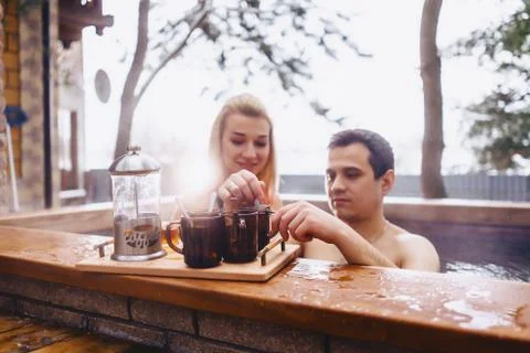 Couple drinking hot tea while sitting in the winter outside hot spa Stock Photos
