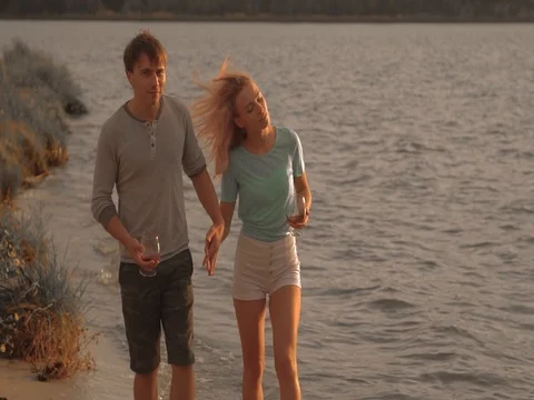 A couple drinking wine and walking down the beach at sunset Stock Footage 80599093