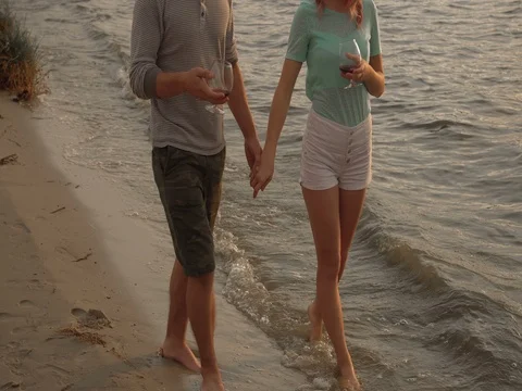 A couple drinking wine and walking down the beach at sunset Stock Footage 80599275