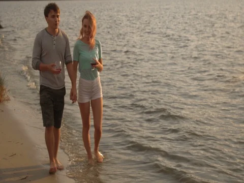 A couple drinking wine and walking down the beach at sunset Stock Footage 80599290