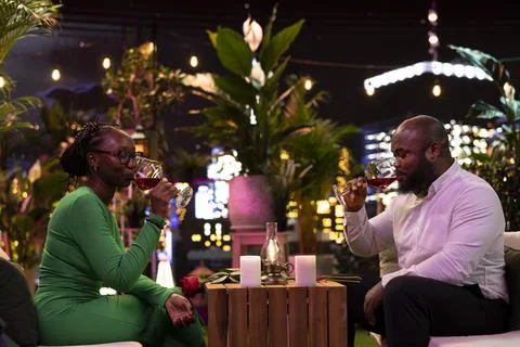 Couple drinks red wine during relaxed rooftop restaurant date at night Fotos Stock
