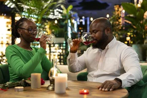 Couple drinks red wine during relaxed rooftop restaurant date at night Fotos Stock