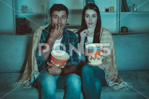 The couple eating popcorn and watch a horror movie on the sofa Stock Photos