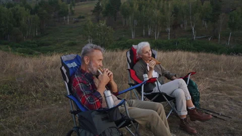 Couple eats sandwiches and drinks tea sitting on camping chairs Stock Footage 319887038