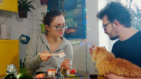 The couple eats sushi at home in the kitchen, the girl offers to try sushi to Stock Footage 128000188
