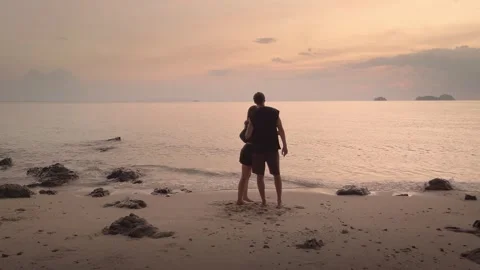 A couple embraces on ocean beach under orange sunset, symbolizing love. Their Stock Footage 270417810