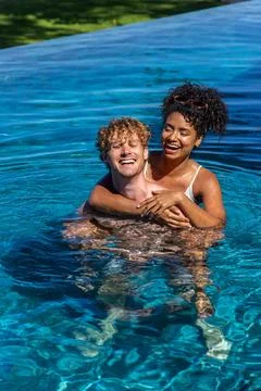 Couple embracing and laughing while standing in infinity pool with sunglasses Stock Photos