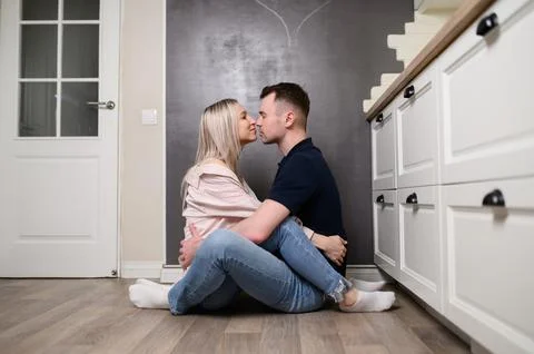 Couple embracing while sitting on kitchen floor, expressing affection, care, and Stock Photos